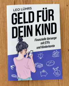 Das Buch „Geld für dein Kind“ von Leo Lührs auf einem Holzboden